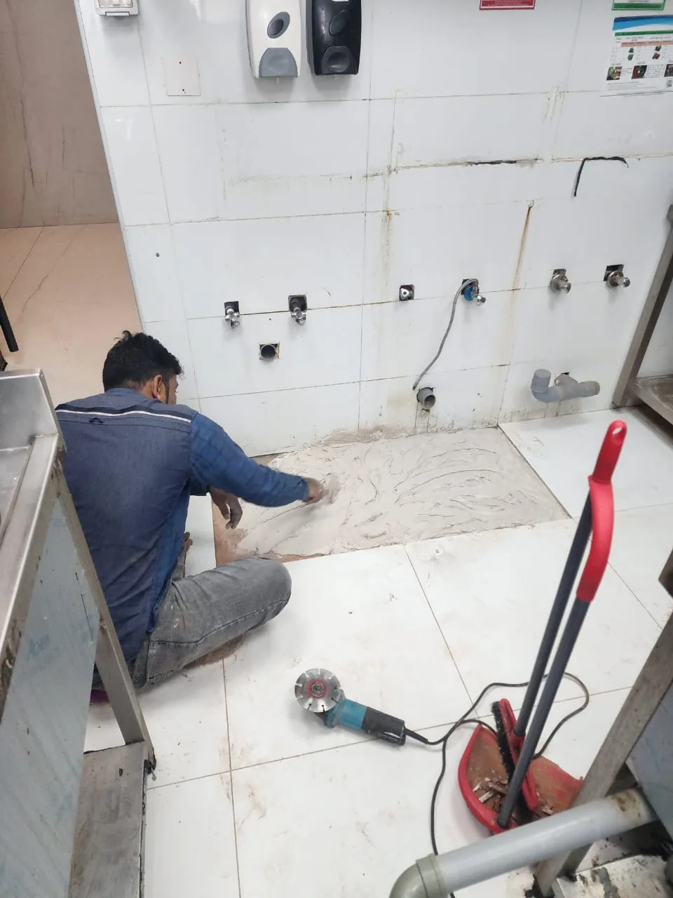 Technician carrying out drain blockage repair work in a tiled service area Technician carrying out drain blockage repair work in a tiled service area