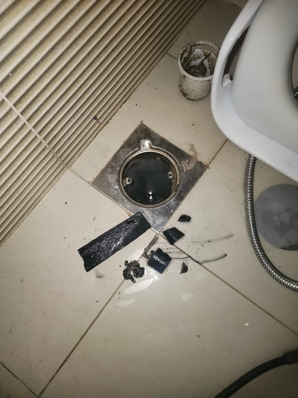 Opened floor drain with removed blockage debris beside bathroom fixture Opened floor drain with removed blockage debris beside bathroom fixture